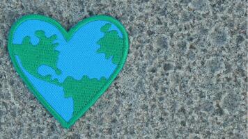 Green and blue Earth-patterned heart embroidery on sandy beach, positioned to the left with copy space on the right. Natural light, perfect for Earth Day and eco-friendly concepts. photo