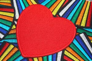 Handmade embroidery of a large red heart crafted from thread and fabric resting on a vibrant rainbow-colored textile background. Perfect for Valentine Day weddings and romantic celebrations photo