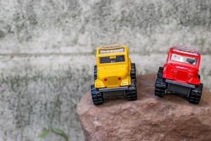 Creative miniature scene of two 4x4 pickup trucks, one yellow and one red, parked side by side on rugged brown rocks, simulating an adventurous journey. Space left on the left for text. photo