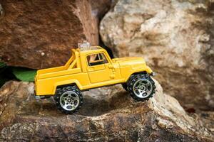 Creative miniature scene of a small yellow 4x4 pickup truck parked on rugged rocky terrain, appearing to stop at the edge of a cliff. Exciting tiny adventure concept with challenging obstacles. photo