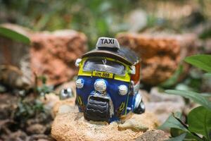 Close-up of colorful miniature Thai tuk-tuk sculpture placed centrally with a rustic, soft-focus background of brown stone, evoking ancient countryside vibes. Natural light, cultural charm. photo