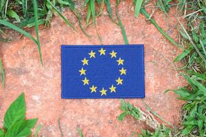 Eco friendly European Union flag, hand embroidered with natural fabric, placed on ancient stone surrounded by greenery. Promoting unity, sustainability, and environmental awareness in Europe. photo