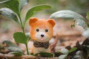 A tiny orange clay dog figurine with big eyes and tongue out, happily sitting under a small tree among green grass. Soft-focus background, playful natural concept representing love for nature. photo