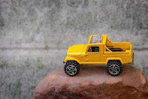 Creative miniature scene of a yellow 4x4 pickup truck placed on rugged brown rocks, simulating a mountain adventure. Captured from a high 45-degree angle with soft-focus background. photo