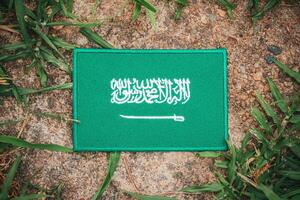 Eco-friendly Saudi flag made from fabric, placed on natural rock with leaves and grass around. Top-view from Middle East theme. Ideal for environmental and Earth Day content. photo