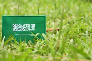 Green-themed Saudi flag made from embroidered fabric, placed on natural grass with open space for text. Ideal for eco concepts and the Middle East Green Initiative. photo