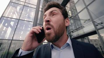 Mad middle-aged Caucasian business man shouting scolding yelling angry to mobile phone conversation arguing problem argument quarrel near office building in city businessman male work failure fury job video