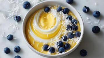 Smooth mango yogurt with a swirl of cream and decorated with blueberries and coconut flakes. photo