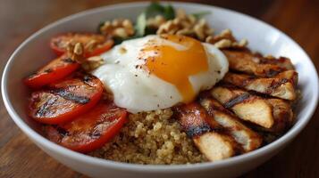 A nutritious bowl filled with grilled chicken, quinoa, a poached egg, and sliced tomatoes. photo