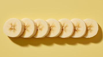 Ripe banana slices are lined up on a bright yellow surface, showcasing their texture and color. photo