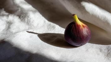 A vibrant fig sits alone on smooth white fabric, illuminated by gentle sunlight in a serene setting. photo