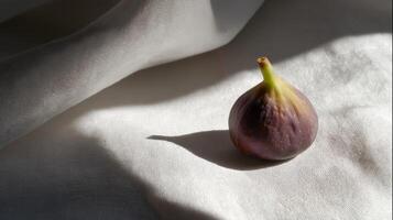 A single ripe fig sits on a light fabric, illuminated by soft sunlight creating delicate shadows. photo