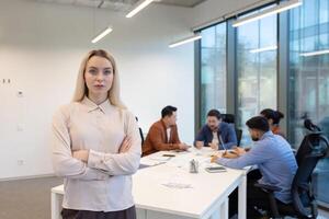 A determined businesswoman stands confidently in front of her team during a meeting, embodying leadership and focus in a modern office setting. photo