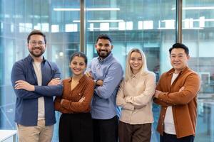 Diverse business team standing together, arms crossed, smiling confidently in an office setting with a modern glass wall. photo