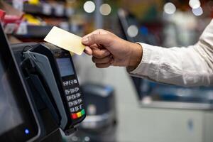 A hand holding a credit card over a payment terminal during a purchase in a store. Contactless payment concept. photo