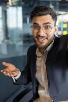 Successful businessman uses phone for call, man in business suit works inside office, looks at camera, remote business meeting, records message. photo
