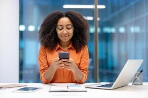 Smiling woman using a smartphone at her office desk, with a laptop and tablet in the background. photo