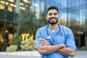 Smiling healthcare professional in scrubs with a stethoscope, standing outdoors in front of a modern building. photo