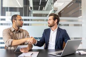 Two businessmen shaking hands in a modern office setting, likely after a successful deal or agreement. Focus on collaboration and teamwork. photo