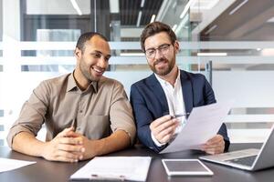 Two businessmen are reviewing documents in a modern office, discussing plans, and smiling. Collaboration and business are key themes. photo