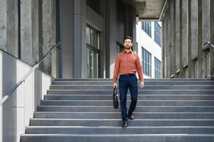 A businessman walks down the steps of a modern building, carrying a briefcase, exuding a sense of purpose. photo