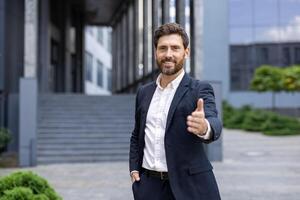 A smiling businessman extends a hand in greeting, dressed in a stylish suit, ready to shake hands. This picture is set outdoors in a business-like environment. photo