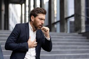 A man in a suit coughs and clutches his chest, appearing ill on outdoor steps. photo