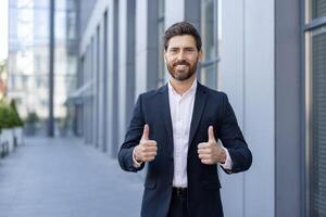 A successful businessman gives a thumbs up, expressing approval and satisfaction while standing in front of an office building. photo