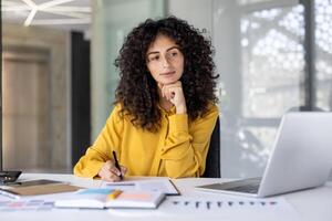 Serious and confident businesswoman working with documents and reports. Woman thinking about current financial investment tasks, preparing report, and filling tax forms while sitting inside office. photo