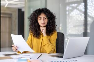 A thoughtful accountant reviews paperwork in a modern office setting, looking for discrepancies and ensuring compliance photo