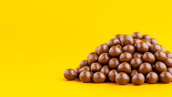 Chocolate candies on yellow. A vibrant pile of shiny chocolate candies rests on a bright yellow surface, making an enticing display. photo