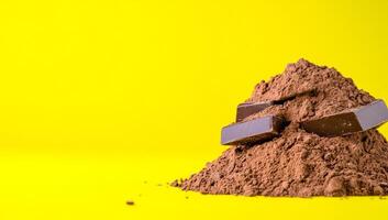 Chocolate on yellow backdrop. Dark chocolate bars rest atop a mound of cocoa powder against a bright yellow backdrop, creating a rich, inviting look. photo