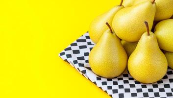 Pears on patterned cloth. Fresh, ripe pears are stacked neatly on a black and white patterned cloth against a bright yellow backdrop. photo