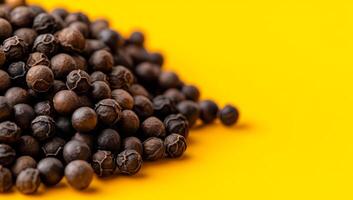 Black pepper seeds on bright background. A close-up view of black pepper seeds resting on a vibrant yellow surface, highlighting their texture and color. photo