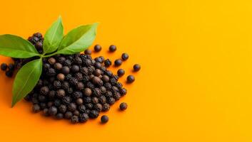 Peppercorns and leaves on orange. Black peppercorns dot a bright orange background, complemented by fresh green leaves for added freshness. photo