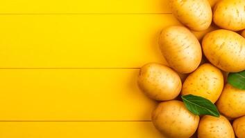 Fresh potatoes on yellow. Fresh potatoes with green leaves are beautifully arranged on a bright yellow background, highlighting their appeal. photo