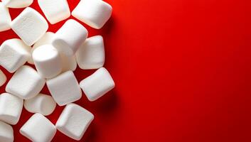 Marshmallows scattered on red background. White marshmallows are arranged haphazardly on a vibrant red surface, creating a playful contrast in colors. photo
