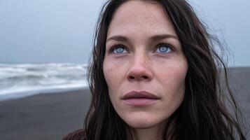 A Pensive Woman Gazes at the Ocean on a Dramatic Beach. Her Blue Eyes Reflect the Moody Seascape, Evoking a Sense of Calm and Cont photo
