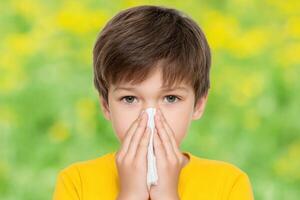 Child with Allergies A Portrait of a Young Boy Sneezing and Suffering from Seasonal Allergies. He is holding a tissue to his nose photo
