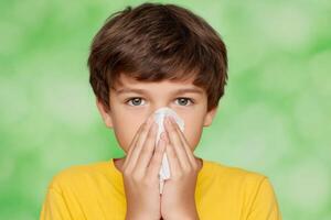 A young boy with a cold, covering his nose with a tissue. He looks unwell and sad. The image shows common cold symptoms and chil photo