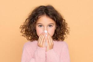 A young girl with a cold, gently blowing her nose with a tissue. The image conveys feelings of sickness, the need for care, and th photo