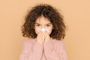 A young girl with a cold, covering her nose with a tissue. The image depicts symptoms of illness, focusing on health and wellness photo
