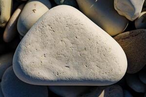 Discover the tranquility of a smooth, light-colored beach stone in this close-up image. Its natural texture and shape offer a calming touch, ideal for various design and creative projects. photo