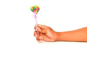 A child's hand holds a colorful heart-shaped lollipop against a white background, symbolizing sweetness and innocence photo