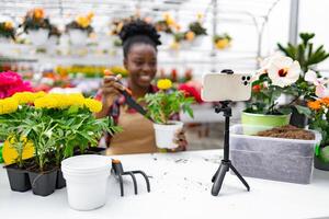 A smiling woman of African descent demonstrates gardening techniques while filming a tutorial on a smartphone set up on a tripod. photo