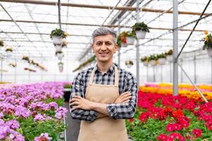 A smiling man in an apron stands in a greenhouse, surrounded by colorful flowers. photo