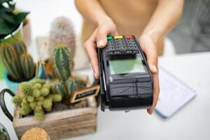 A florist offers a point-of-sale device at a counter with cacti visible in the background, promoting commerce. photo