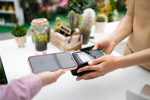 A customer pays with a phone using contactless payment at a florist shop. Various plants are visible in the background. photo