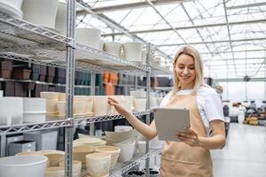 A shop assistant with a tablet inspects shelves stocked with various flowerpots, preparing for inventory. photo