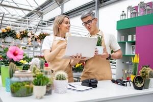 A florist and a shop owner, both Caucasian, look at a laptop. The image captures a scene of a sale table. photo
